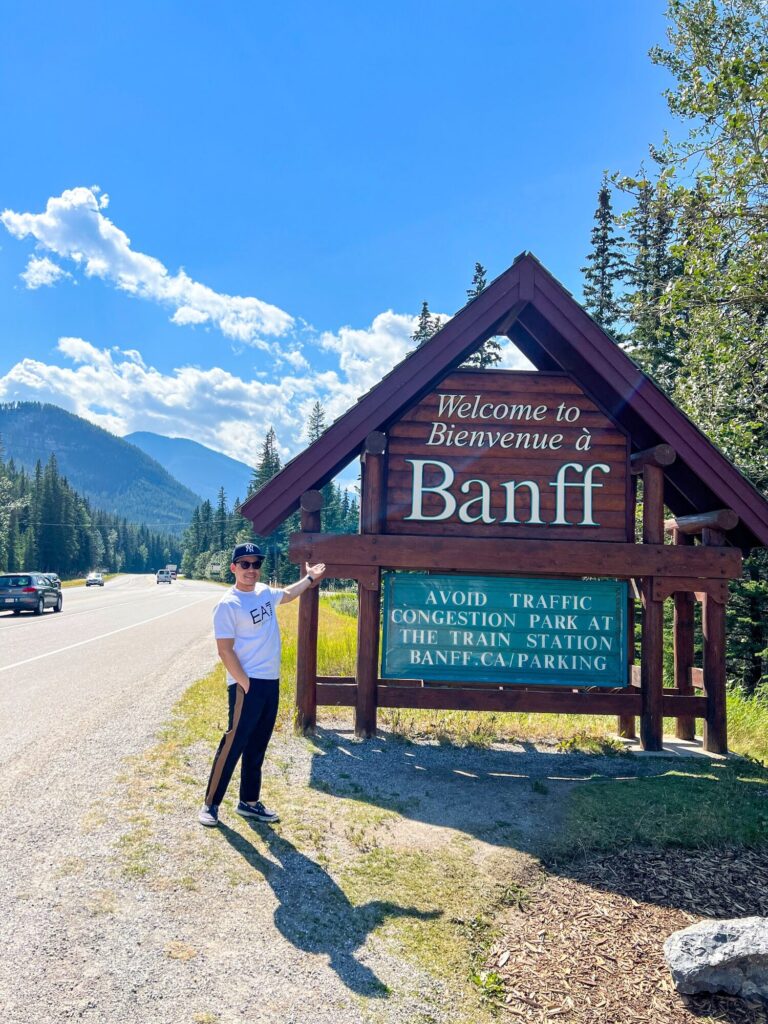Traveler standing beside the Welcome to Banff sign in Banff National Park, Alberta.